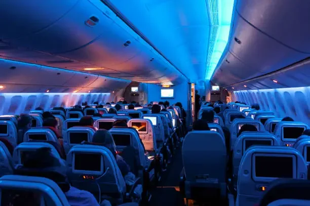 Passengers seated in a darkened airplane cabin, seatback screens glowing